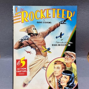 May include: A vintage comic book cover for "The Rocketeer" by Dave Stevens. The cover features a costumed character in a helmet and goggles, with a retro aviation theme. The cover also includes the text "all 5 action chapters".