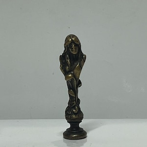 Puede incluir: Sello de cera de color bronce que representa un busto de mujer con pelo largo y una serpiente. El sello tiene un diseño detallado y una base oscura, adecuado para añadir un toque de elegancia a la correspondencia o a las manualidades.