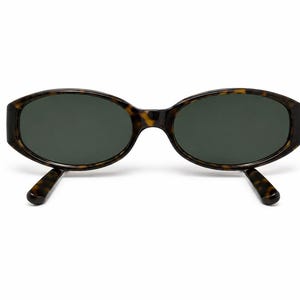 May include: Oval-shaped sunglasses featuring a brown and black tortoiseshell pattern frame with dark green tinted lenses. The eyewear has a thick, rounded rim design and matching tortoiseshell temples that extend outward from the frame front.
