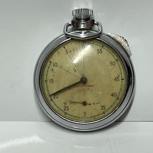 Könnte beinhalten: Eine silberfarbene Vintage-Stoppuhr mit cremefarbenem Zifferblatt. Sie hat schwarze Ziffern und Zeiger, mit dem Wort "YACHTSMAN" auf dem Zifferblatt. Die Stoppuhr ist zum Messen von Ereignissen konzipiert. Durchmesser ca. 5 cm.