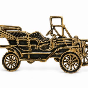 Op de afbeelding: Een decoratief beeldje van goudkleurig en zwart metaal in de vorm van een vintage open auto. Het stuk is voorzien van gedetailleerde spaakwielen, een stuurwiel, een ingeklapte dakconstructie en gestructureerde zittingen in reliëf.