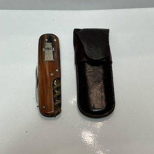 May include: A brown and silver pocket knife with a corkscrew and a leather sheath. The knife has a lighthouse design on the handle and the word "Balcke" engraved on it.