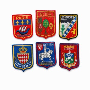 Pode incluir: Uma coleção de seis emblemas bordados em forma de escudo com vários designs e textos, incluindo Paris, Blida, Les Houches, Monaco, Rouen e Fécamp. Cada emblema exibe imagens heráldicas coloridas e um trabalho de costura detalhado.