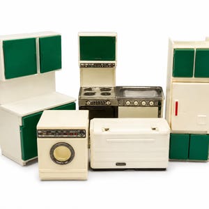 Pode incluir: Um conjunto de eletrodomésticos de cozinha para casa de bonecas, incluindo um armário alto, uma unidade de fogão e pia, um frigorífico, uma máquina de lavar e uma arca congeladora. As peças são esbranquiçadas com portas e detalhes verde-escuros.