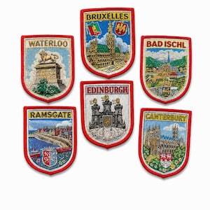 May include: A collection of six shield-shaped embroidered patches with red borders. Each patch features a city name including Waterloo, Bruxelles, Bad Ischl, Ramsgate, Edinburgh, and Canterbury, accompanied by detailed thread-stitched illustrations.