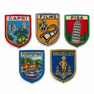 Può includere: Cinque toppe ricamate a forma di scudo. La fila superiore mostra Capri con rocce costiere, una bobina cinematografica con la scritta FILMS e la Torre di Pisa. La fila inferiore mostra il porto di Portofino e la statua di BRUXELLES.