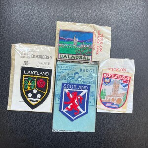 Può includere: Una collezione di distintivi souvenir ricamati vintage, tra cui Lakeland, Balmoral, Scozia e Oxford. Ogni distintivo presenta un design unico ed è confezionato nella sua confezione originale. I distintivi sono di varie forme e colori.
