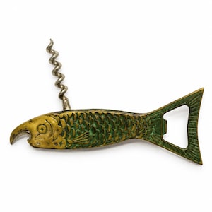 May include: A fish-shaped metal bottle opener and corkscrew combination tool. The body features a textured scale pattern with a green and gold finish. The corkscrew is positioned on the top of the fish, while the bottle opener is integrated into the tail.