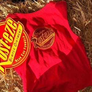 May include: A red vest top with a circular yellow and red graphic  vest top is sleeveless and has a matching graphic on the back. The items are on a bed of straw.