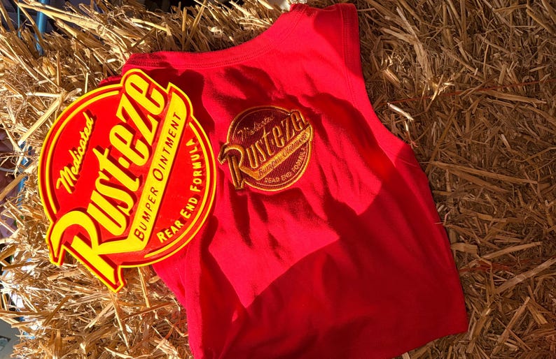 May include: A red vest top with a circular yellow and red graphic  vest top is sleeveless and has a matching graphic on the back. The items are on a bed of straw.
