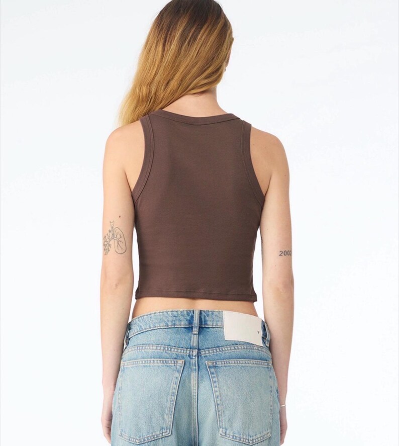 May include: A brown ribbed tank top with a scoop neckline. The cropped top is paired with light blue denim jeans. The model is facing away from the camera.
