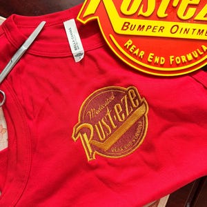 May include: A red vest top with a circular yellow and red graphic  vest top is sleeveless and has a matching graphic on the back. The items are on a bed of straw.
