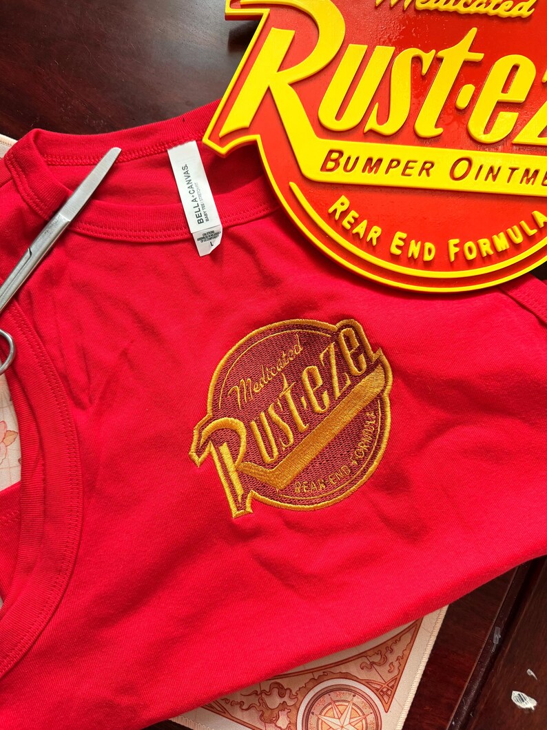 May include: A red vest top with a circular yellow and red graphic  vest top is sleeveless and has a matching graphic on the back. The items are on a bed of straw.
