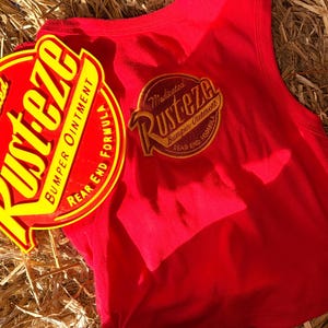 May include: A red vest top with a circular yellow and red graphic  vest top is sleeveless and has a matching graphic on the back. The items are on a bed of straw.