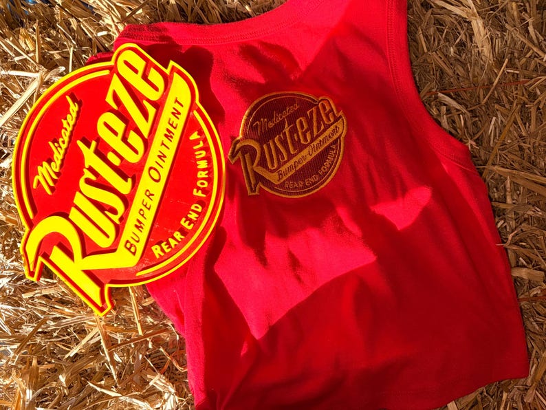 May include: A red vest top with a circular yellow and red graphic  vest top is sleeveless and has a matching graphic on the back. The items are on a bed of straw.