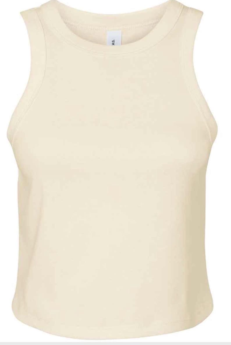 May include: Cream-colored tank top with a rounded neckline and sleeveless design. The top is made of a soft, smooth fabric. The garment has a simple, minimalist style, suitable for casual wear.