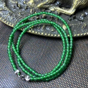 May include: A vibrant green beaded necklace with a silver clasp. The necklace is composed of small, round beads, creating a layered effect. The beads are a rich, emerald green color, and the clasp is a bright silver.