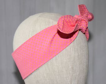 May include: A pink headband with a bow, adorned with a repeating pattern of small orange dots. The headband is displayed on a mannequin head against a light gray background.