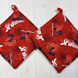 Puede incluir: Dos agarraderas rojas con el tema de Spider-Man. Las agarraderas presentan un patrón repetido de Spider-Man, telarañas y las palabras "Spider-Man" y "Wall-Crawler" en blanco. Cada agarradera tiene un lazo rojo para colgar.