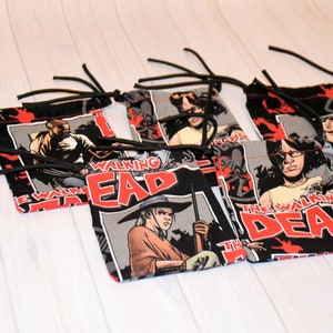 May include: Small drawstring bags with comic book panels and the text "THE WALKING DEAD" in red. The bags have a black background with red accents and black drawstrings. The bags are made of fabric.