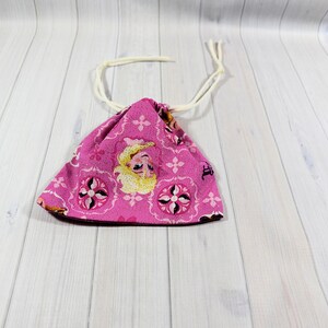 May include: A pink drawstring bag featuring a cartoon character design. The bag has a repeating floral pattern and a white drawstring closure. The bag is made of fabric and is likely used for storage or carrying small items.