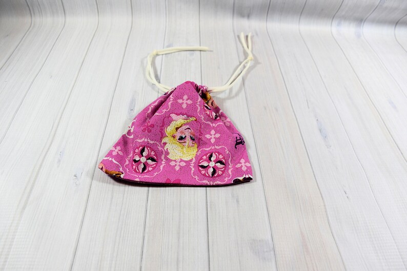 May include: A pink drawstring bag featuring a cartoon character design. The bag has a repeating floral pattern and a white drawstring closure. The bag is made of fabric and is likely used for storage or carrying small items.