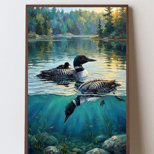 May include: A framed wall art print depicting a loon with a chick on its back swimming on a lake surface, while another loon dives beneath the clear blue water. The scene includes a forest shoreline, rocky lake bed, and sunlight.