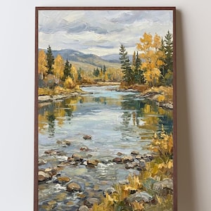 May include: An oil painting in a dark brown frame depicting a river landscape with visible brushstrokes. The scene features a flowing stream with scattered rocks in the foreground, surrounded by yellow autumn trees and distant mountains under a cloudy sky.