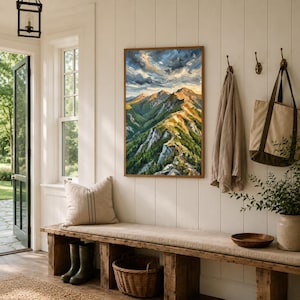 May include: A rectangular framed oil painting depicting a mountain range with green slopes, rocky peaks, and a cloudy sky. The artwork features a vibrant color palette of deep greens, earthy browns, and bright blues, displayed on a white wall.