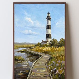 May include: An oil painting in a brown frame depicting a tall, black and white striped lighthouse standing near a wooden boardwalk that winds through a marshy landscape with tall grasses, purple wildflowers, and a light blue sky with clouds.