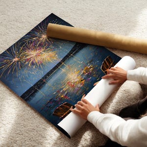 May include: A rectangular art print featuring a dark night sky filled with vibrant, multi-colored fireworks exploding above a calm body of water. The scene includes reflections of the light on the water surface and a brown cardboard shipping tube.