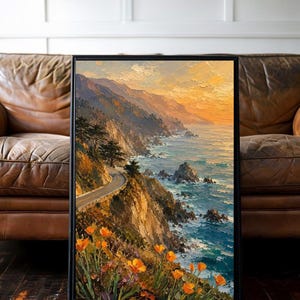 May include: Framed landscape art print depicting a coastal road winding along cliffs, with the ocean on the right. The artwork features a vibrant sunset, orange poppies, and a black frame. The painting style is impressionistic.