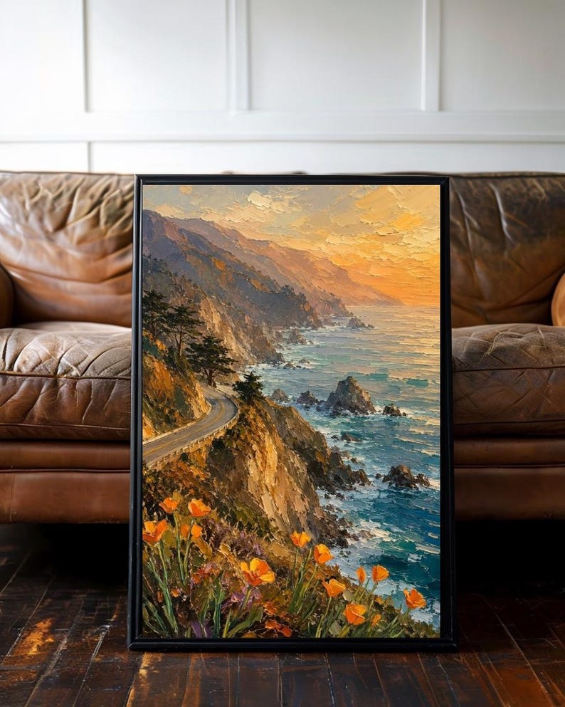 May include: Framed landscape art print depicting a coastal road winding along cliffs, with the ocean on the right. The artwork features a vibrant sunset, orange poppies, and a black frame. The painting style is impressionistic.