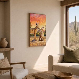May include: A rectangular wall art print featuring an oil painting of two coyotes standing in a desert landscape. The scene depicts a vibrant orange and yellow sunset sky, tall green saguaro cacti, and textured brushstrokes of tan earth.