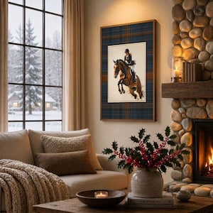 May include: A framed wall art piece featuring a brown horse jumping with a rider in equestrian gear, set against a blue and brown plaid background. The artwork is displayed on a wall next to a stone fireplace and a window with a snowy view.