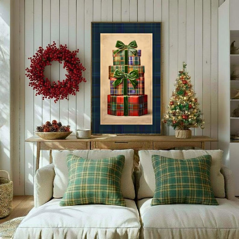 May include: A framed wall art print featuring a stack of three wrapped gift boxes with green bows, displayed above a sofa with two green plaid throw pillows. The artwork is centred on a white panelled wall between a red berry wreath and a small tree.
