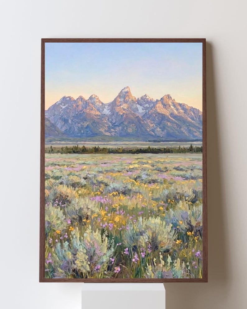 May include: A framed oil painting depicting a mountain range with snow-capped peaks under a soft sunrise sky. The foreground features a vast meadow filled with textured brushstrokes of yellow and purple wildflowers and sage-green shrubs.