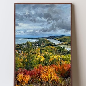May include: An oil painting in a brown frame depicting a landscape with vibrant autumn foliage in shades of red, orange, and yellow. The scene features a dense forest overlooking a body of water under a dramatic, cloudy, grey sky.