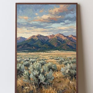 May include: A framed oil painting depicting a vast landscape with sagebrush in the foreground, a golden grassy plain in the midground, and a range of rugged mountains under a cloudy sky with soft pink, blue, and orange hues at sunset.