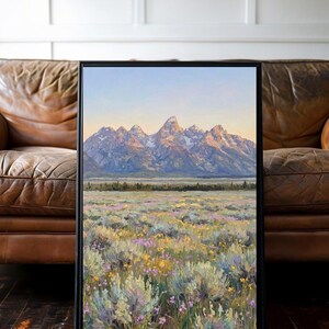 May include: A framed landscape painting featuring a mountain range with snow-capped peaks under a soft sky, overlooking a vast field filled with sagebrush and small yellow and purple wildflowers, rendered in a textured, painterly style.