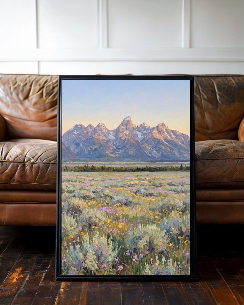 May include: A framed landscape painting featuring a mountain range with snow-capped peaks under a soft sky, overlooking a vast field filled with sagebrush and small yellow and purple wildflowers, rendered in a textured, painterly style.