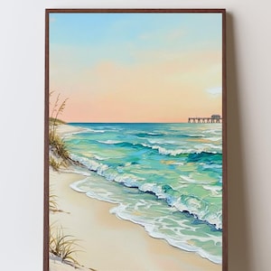 May include: A framed painting of a beach scene. The artwork shows a sandy beach with turquoise waves breaking on the shore. The sky transitions from a soft peach to a light blue. A pier is visible in the distance.