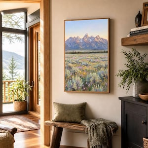 May include: A vertical rectangular wall art print featuring a landscape painting of snow-capped mountain peaks rising above a vast meadow filled with sagebrush, wildflowers, and grasses under a soft, pale blue and golden sunrise sky.
