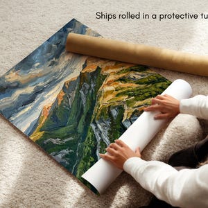 May include: A square art print featuring an oil painting of a mountain landscape with deep green slopes, rocky peaks, and a stormy blue sky. The print is partially rolled, showing a white underside, and is accompanied by a brown cardboard tube.