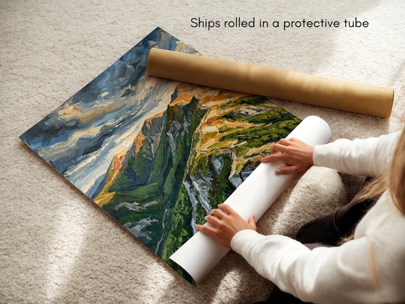 May include: A square art print featuring an oil painting of a mountain landscape with deep green slopes, rocky peaks, and a stormy blue sky. The print is partially rolled, showing a white underside, and is accompanied by a brown cardboard tube.