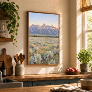 May include: A framed vertical wall art print depicting a landscape with a vast field of wildflowers in the foreground and jagged, snow-capped mountain peaks under a soft, pale sky in the background, displayed on a light-colored interior wall.