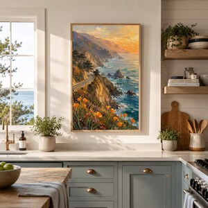 May include: A framed landscape painting depicts a coastal scene with a winding road along a cliffside. The artwork features vibrant orange flowers, a blue ocean, and a sunset sky with warm yellow and orange hues. The painting is displayed in a kitchen setting.