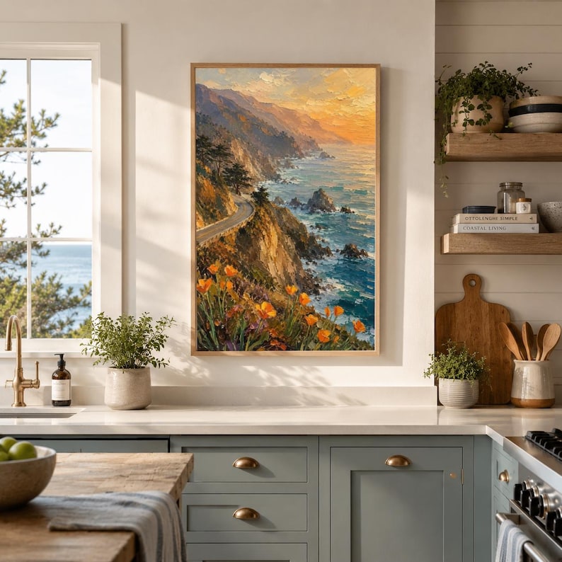 May include: A framed landscape painting depicts a coastal scene with a winding road along a cliffside. The artwork features vibrant orange flowers, a blue ocean, and a sunset sky with warm yellow and orange hues. The painting is displayed in a kitchen setting.