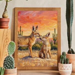 May include: A framed oil painting featuring two foxes in a desert landscape at sunset. The textured brushstrokes depict the foxes standing on sandy ground with cacti in the background under a vibrant orange and pink sky in a wooden frame.