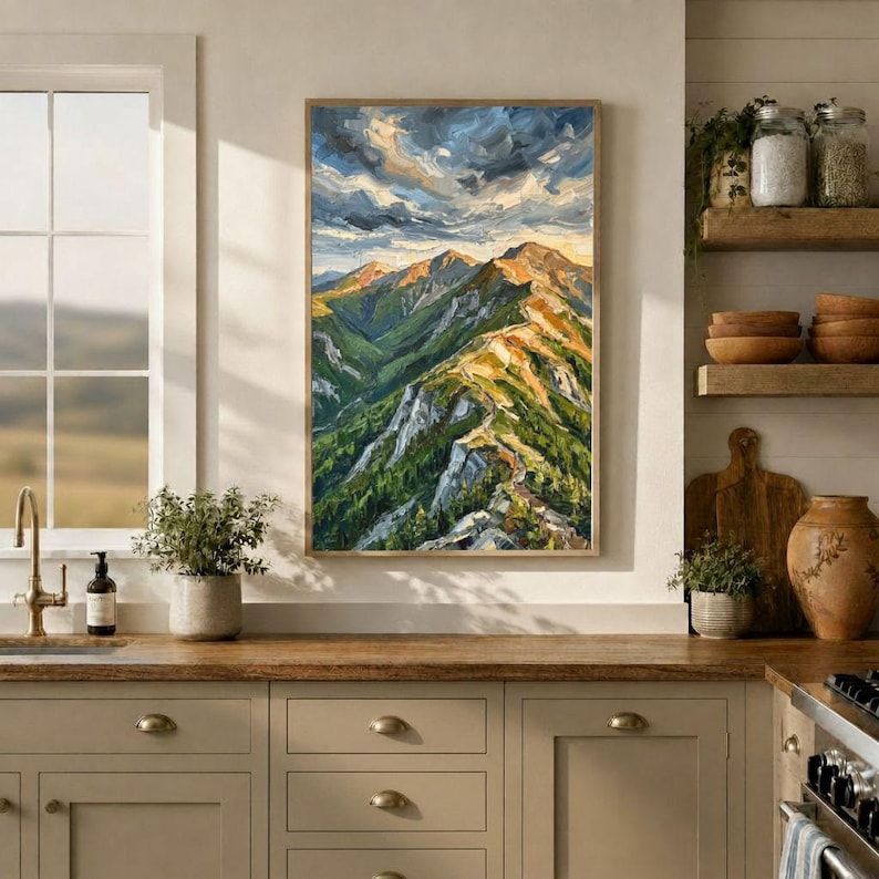 May include: A vertical oil painting depicting a mountain range with green slopes, rocky peaks, and a dramatic sky with swirling clouds in shades of blue, white, and gold, displayed in a kitchen setting above a wooden countertop.
